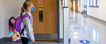 Student walking in school hallway wearing a mask and backpack