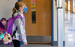 Student walking in school hallway wearing a mask and backpack